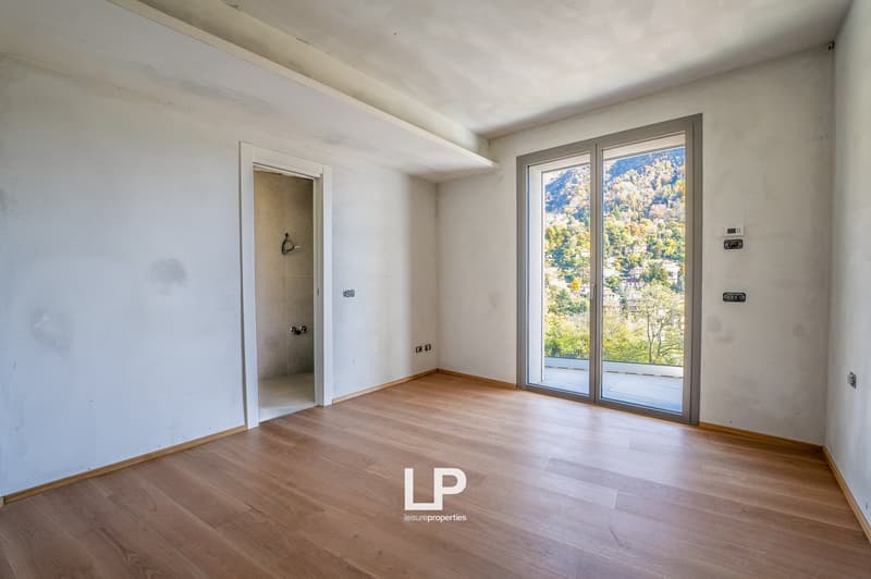 Spacious empty room, sliding glass doors leading to balcony, wooden floor, large windows with balcony, white walls, mountain view outside