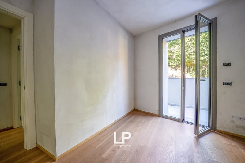 white walls, wooden floor, double glass doors leading to balcony, two power outlets on wall
