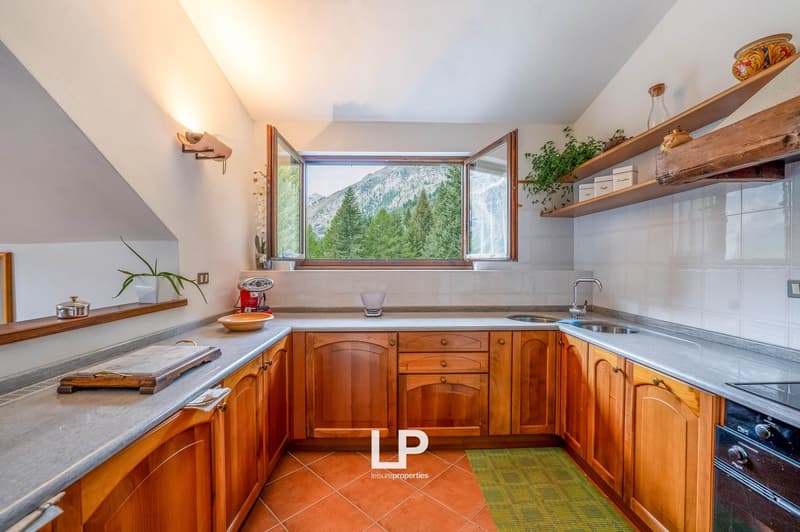 Modern kitchen with wooden cabinets, granite countertops, sink, faucet, shelves, tiled floor, window with a view of mountains.