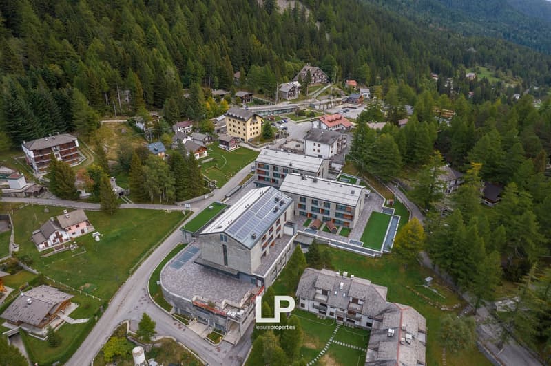 cluster of buildings, stone and wood exterior, nestled in mountains, large road, grassy areas, solar panels on some buildings