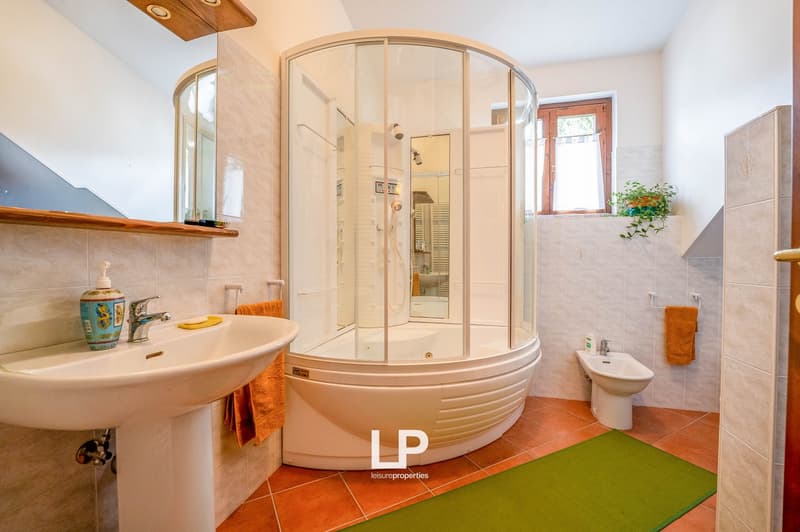 glass enclosed shower, white sink, wooden cabinet, red tile floor