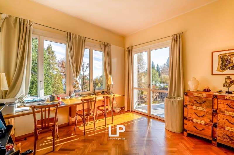 Wooden floor, large windows with curtains, desk, chairs, wooden chest of drawers, trash can, lamp, picture frame
