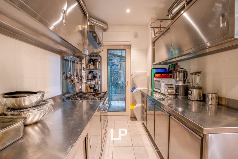stainless steel counter, stainless steel cabinets, gas stove, white tiled wall, sink, dish washer, washing machine, various kitchen utensils