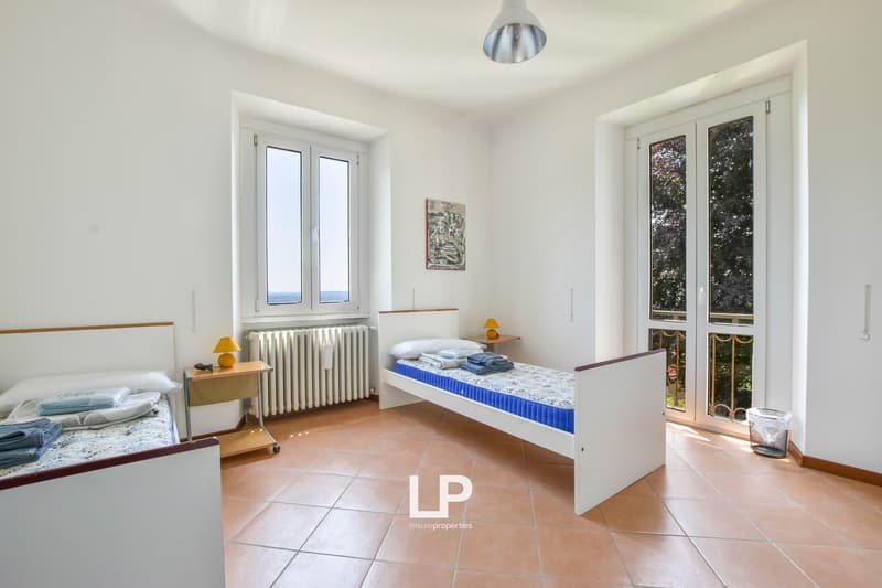 Two beds, nightstands, lamps, radiator, picture on the wall, sliding doors leading to a balcony