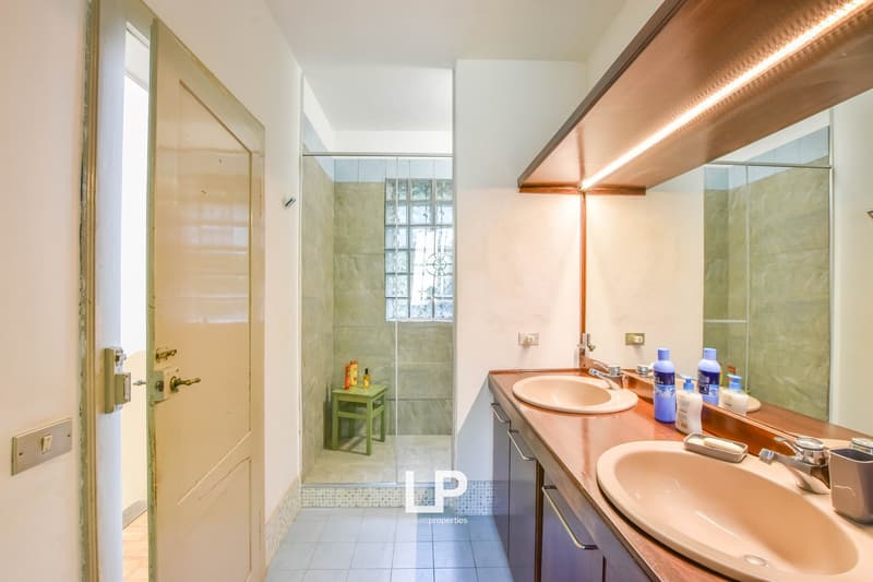 Modern bathroom with double sink, shower, large mirror, wooden countertops, and storage cabinets