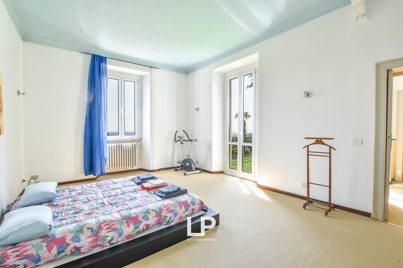 white walls, bedroom with bed, exercise bike, radiator, windows, clothes rack