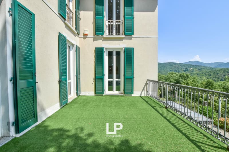 Green shutters, tiled roof, two balconies with railings, artificial grass lawn