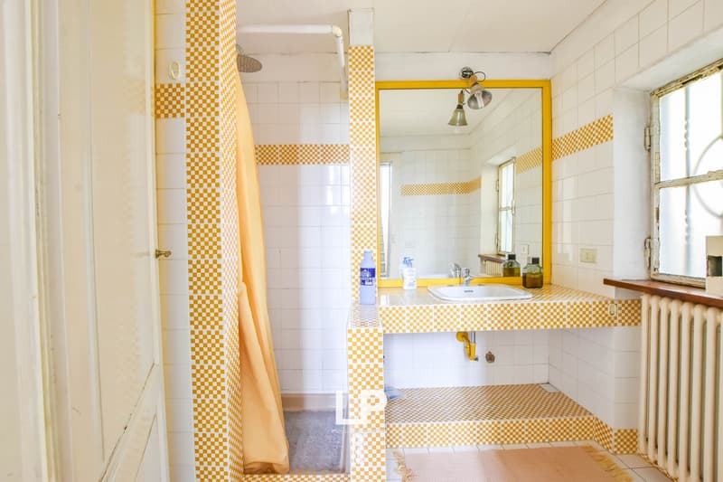 yellow and white tiled bathroom, a shower with shower curtain, a white sink, a mirror, a window