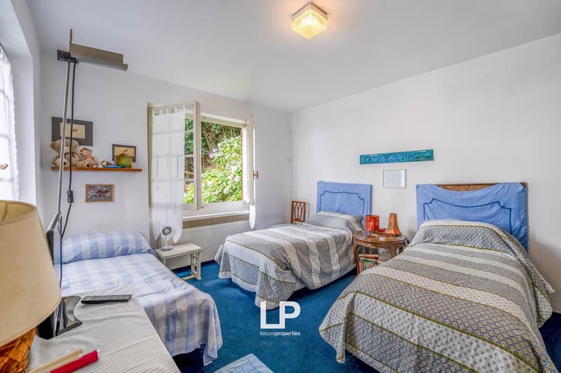 Three single beds, two nightstands, carpet, floor lamp, artwork on the wall, blue carpet