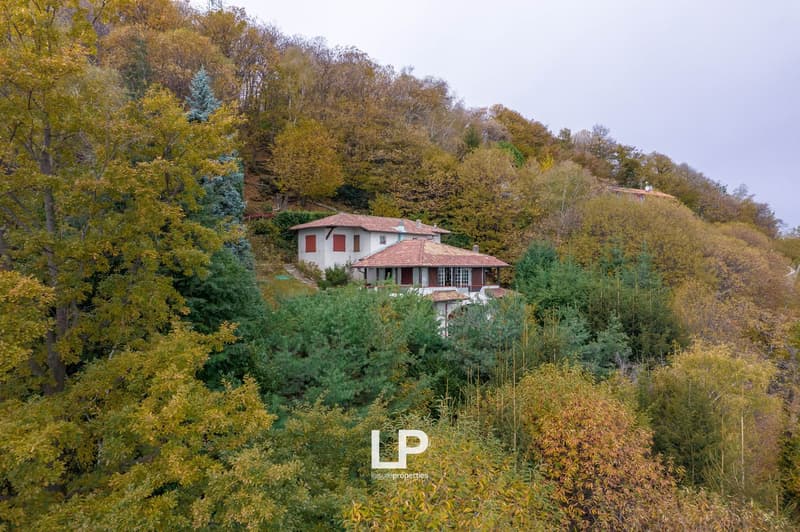 House with a red roof, located on a hillside, surrounded by autumn trees.