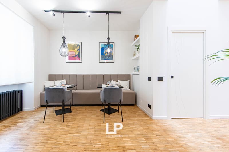 open-plan dining area, wooden floor, white walls, white shelves, grey sofa, hanging lamps, radiator