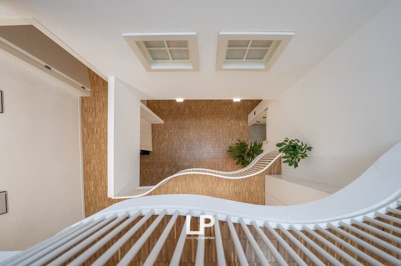 Two story building, large windows, white wooden railing, wooden flooring, white wall, ceiling lights, small garden on upper floor.