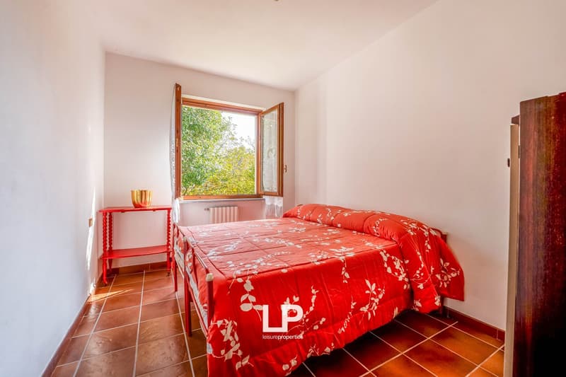 Bedroom with tile floor, single bed, red curtains, bedside table, window with garden view