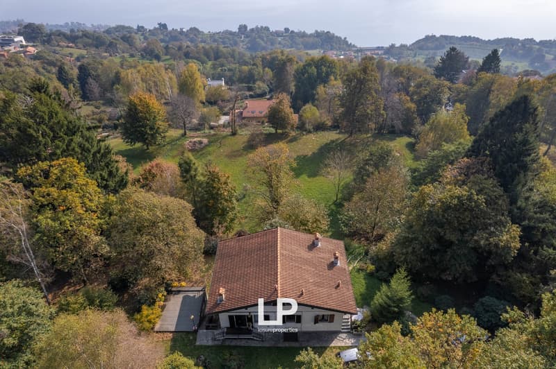 Raised ground floor house, brown roof, driveway, front and back garden, surrounded by trees