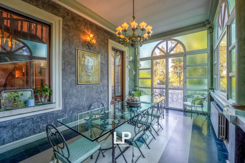 Long glass table, green chairs, chandelier, fireplace, large windows, glass door to balcony