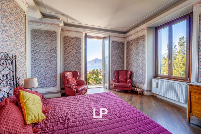 Wooden floor, pink bed with yellow pillow, red chairs, open doors leading to balcony, floral wallpaper, radiator