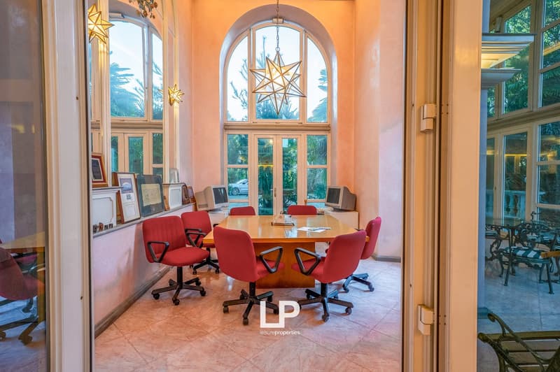 meeting room with a long wooden table, red chairs, windows, monitors, picture frames