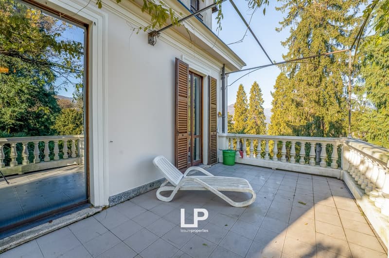 Outdoor balcony with white lounger, glass door, balcony railing, and a green barrel.