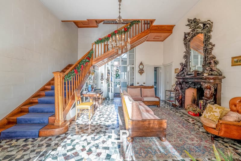 grand wooden staircase, wooden rails, blue carpet, mirror, fireplace, chandelier, white walls, mosaic flooring