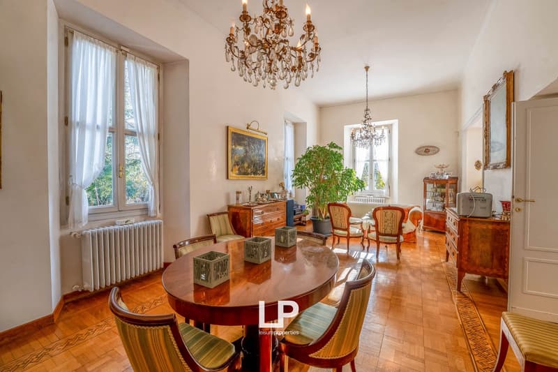 wooden floor, wooden table, chandelier, white walls, curtains, radiator, wooden chair, fireplace, shelves, picture frame, pot, carpet