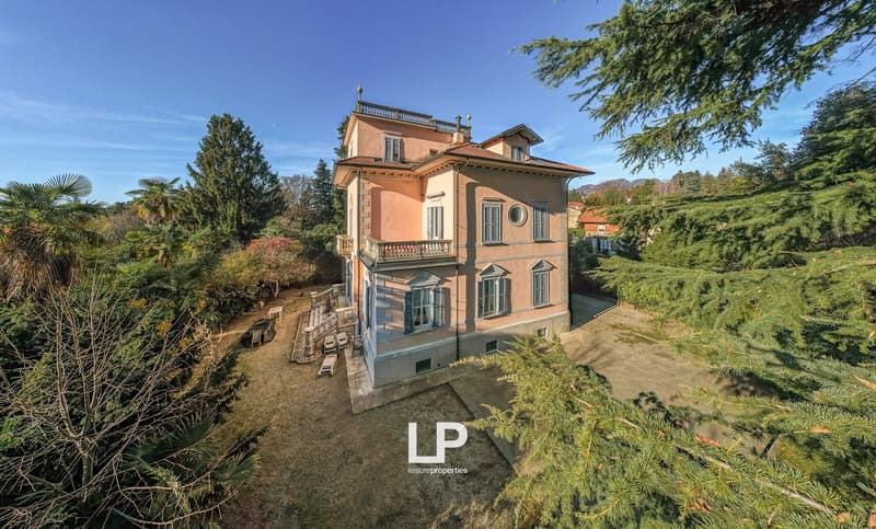 A traditional stone villa set in a large garden, with a large terrace and windows throughout the front, and stairs leading to the terrace at the front