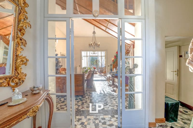 A grand entrance hall with wooden furniture, tiled floor, chandelier, and a window that leads to a balcony