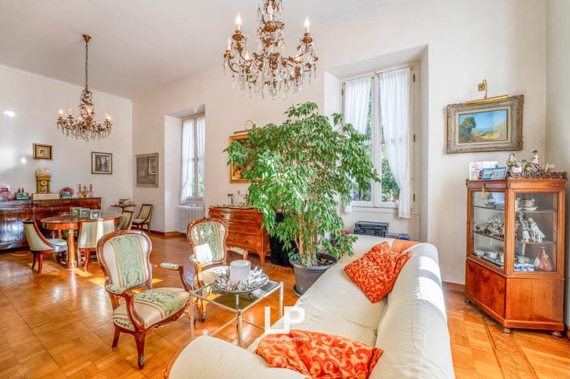 Chandeliers, white sofa, chairs, round table, large potted plant, wood floor, wooden furniture, paintings, wooden cabinet with glass doors.