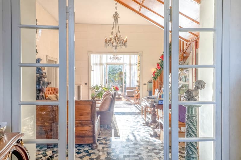 White walls, chandelier, wooden cabinet, couch, chairs, tiled floor, sculpture, open door leading to a balcony