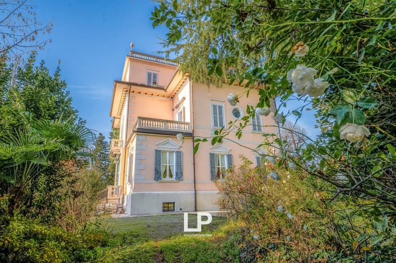 large two-story pink villa, balcony, glass windows, white shutters, large garden with various plants