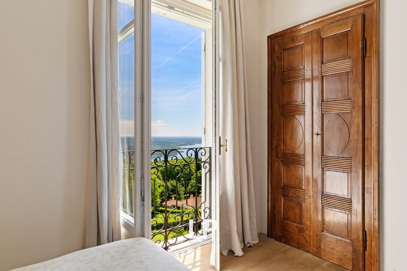 bedroom with bed, white curtains, balcony with railing, view of a landscape