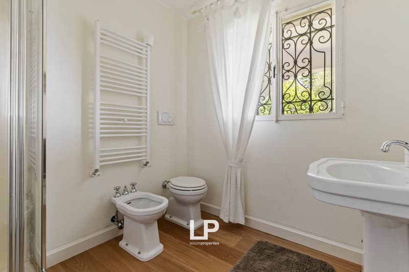 Bathroom with white toilet, bidet, sink, window, shower, and radiator