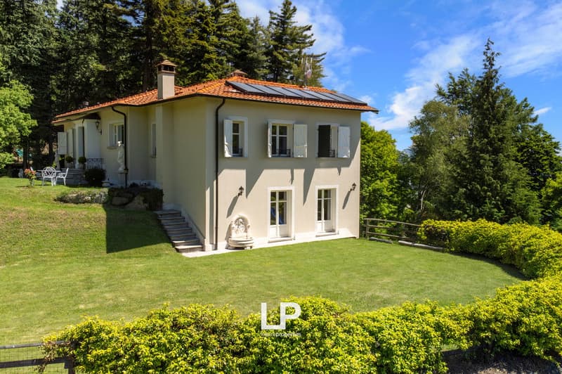 Large house, terracotta roof, solar panels, white shutters, stairs leading up, manicured lawn, trees in background.