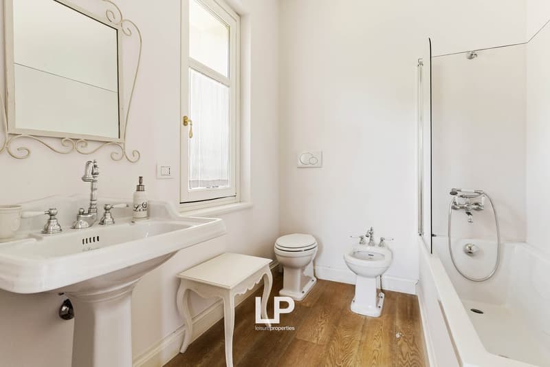 bathroom, white sink, white bathtub, white toilet, white bidet, white mirror with intricate frame, wooden floor, white walls