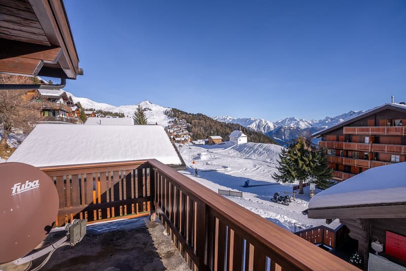 balcony with view of snowy mountains and several buildings, some with snow on their roofs