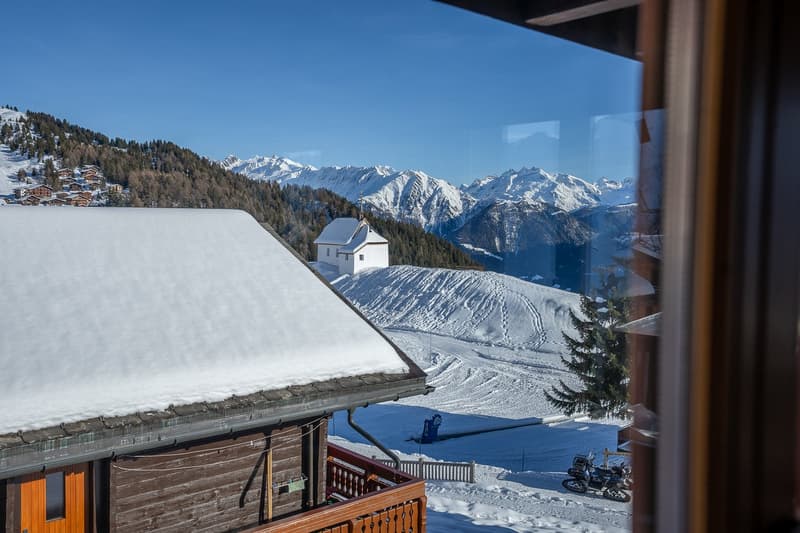 Snow covered rooftop, wooden walls, wooden railings, snowy mountains in the background