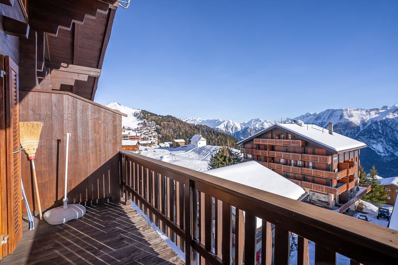 wooden balcony, sweeping views of snow-covered mountains, wooden railings, ski equipment in the distance