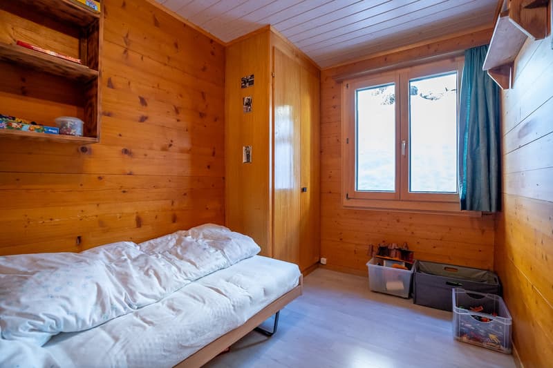 Single bed, wooden wall panels, wooden floor, storage boxes, window, wardrobe, toys on the shelf