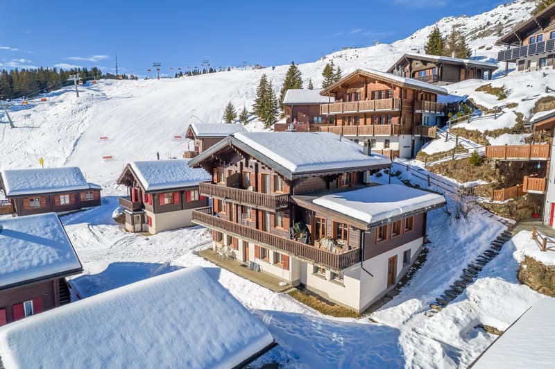 Alpine house with multiple balconies, covered in snow, located on a mountain slope
