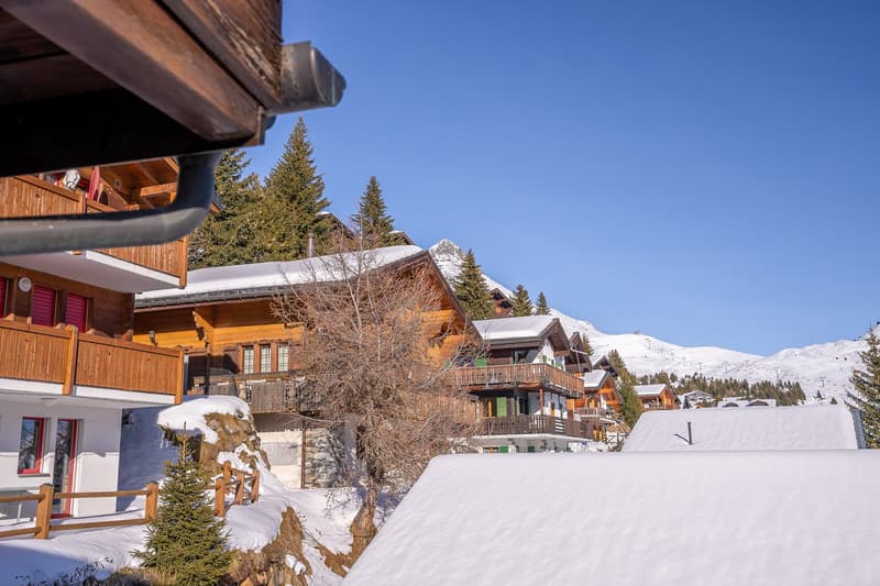 chalet-style wooden buildings with balconies, snowy surroundings, mountains in the background