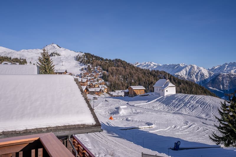 Snowy mountain landscape with village, covered terrace, snow-covered mountains, and ski tracks.