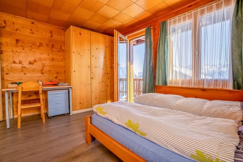 wooden walls, bed with two pillows, desk with chair, small wooden cabinet