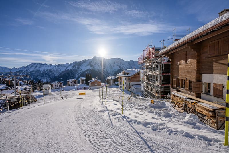 Mountainous snowy landscape with houses and a ski slope in the foreground