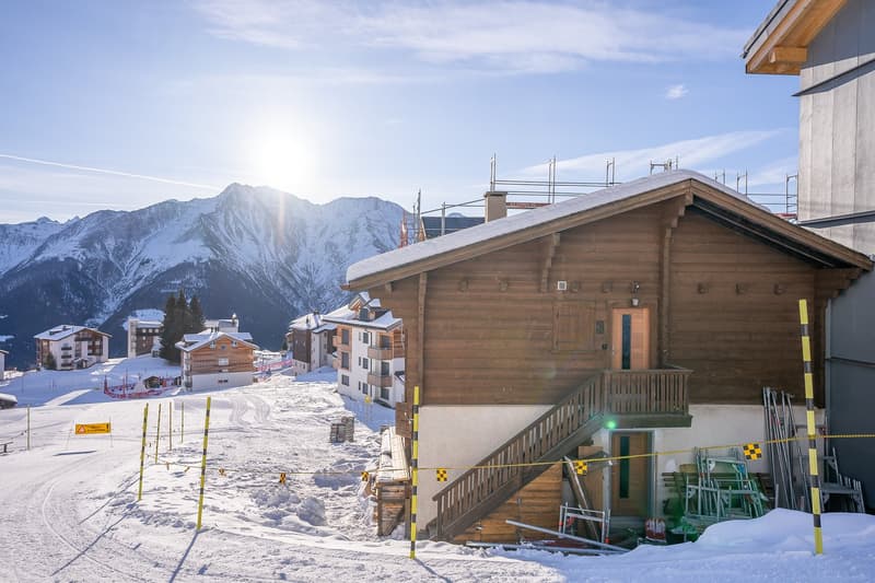 Wooden alpine house in snowy mountainous landscape with snowy mountains