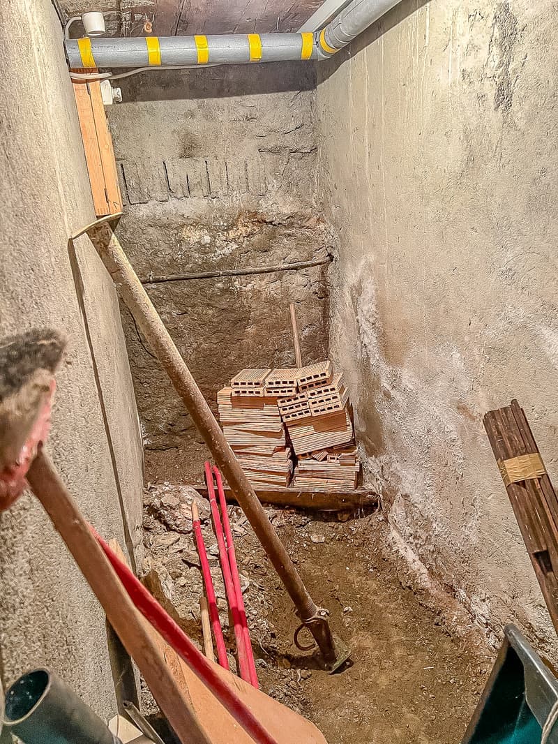 a basement storage area with wooden planks, bricks, a shovel, and an electrical outlet