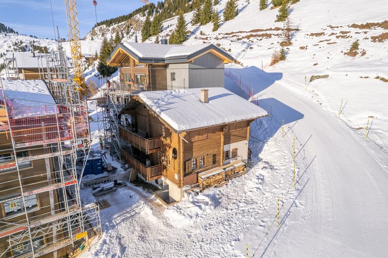 2-story building under construction, wooden facade, snow covered roof, scaffolding on one side, surrounded by snow covered ground