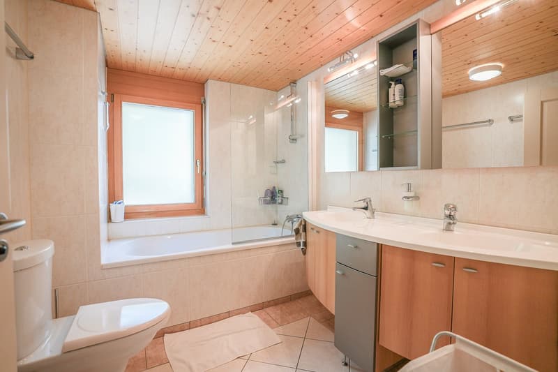 Large bathroom, tub, shower, two sinks, mirror, wooden cabinets, white tiled floor, window with shower curtain