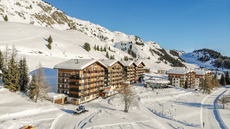 multi-story building with many windows, surrounded by snow and mountains, with trees and a snow covered landscape