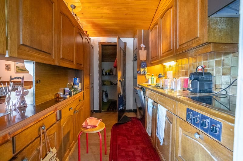 wooden cabinets, tiled wall, countertop, red rug, red stool, dish rack, oven, toaster