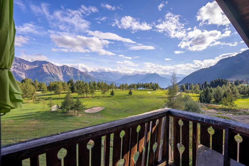Balcony with a view of a golf course, mountains, and sky