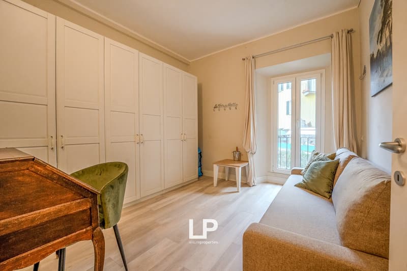 living room with a couch, wooden desk, wooden chair, white wardrobe, white table, double glass door with a balcony view